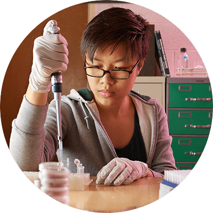 Decorative image; student Kasey Pham during a research experience wearing gloves and using a large pipette with test tubes on the table