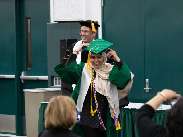 Decorative, candid photo of graduate Mariam Sayed adjusting their cap after receiving an award from Dean Christopher Long (person standing behind Mariam)