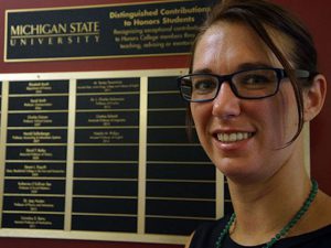 Decorative image of Natalie Phillips smiling wearing glasses in front of an award plaque for Michigan State University Distinguished Contributions to Honors Students listing previous winners