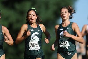 Two Spartan cross country runners racing in green uniforms