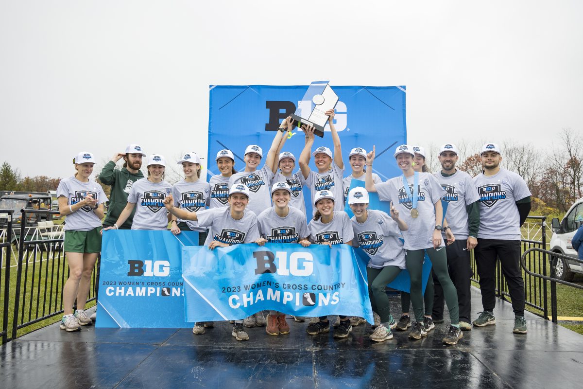The women's cross country team raises their 2023 Big Ten Championship trophy and banner