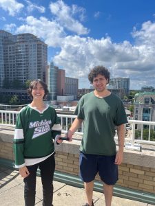 Joanna Gusis and Tony Miklovis holding an award on a city balcony. 