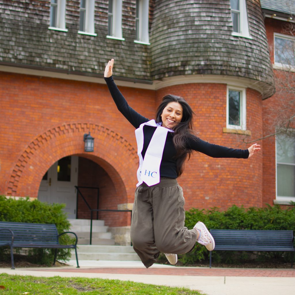 Young woman jumps happily in front of orange building.