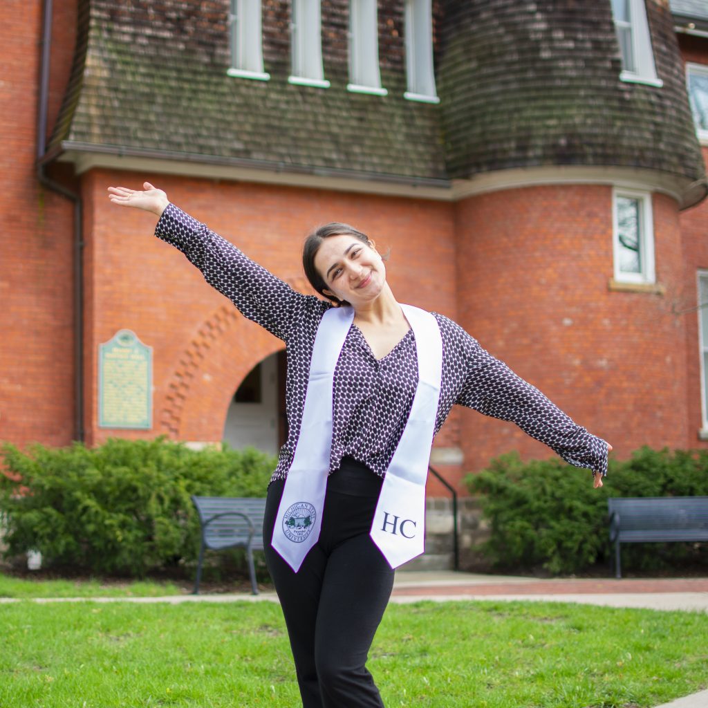 Young woman holds arms out in happiness in front of orange building.