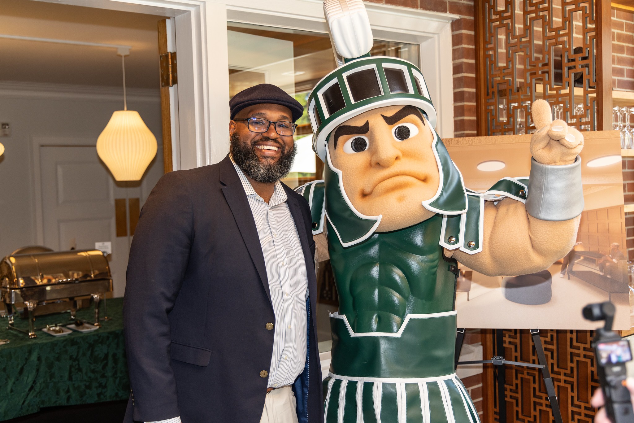 Glenn Chambers stands with Sparty in a room at Cowles House.