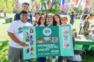 A group of seven college students hold up a green poster board that reads "International Scholars Advisory Board".