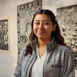 Headshot of Alyssa Briones standing in front of four pieces of black and white artwork.