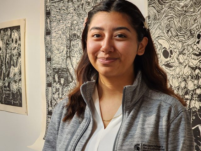 Headshot of Alyssa Briones standing in front of four pieces of black and white artwork.