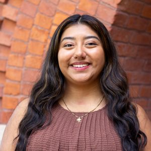Honors College Executive Assistant Alyssa Briones smiling in front of the red brick entrance to Eustace-Cole Hall.