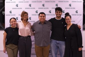 A group of people smiling at camera in front of backdrop that has MSU Honors College logos.