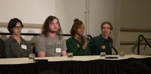 four students sitting at a panel, one student is talking into a microphone