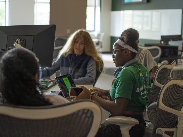 A group of students gather around a table at the Apple Developer Academy in Detroit to brainstorm app ideas.