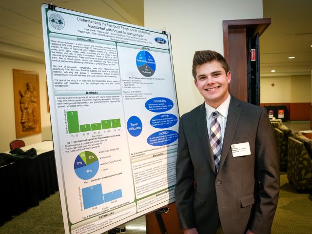 A student stands next to research poster board, smiling at the camera.