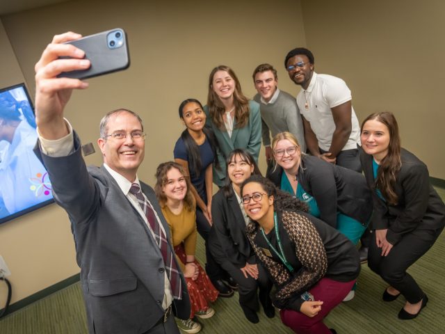 Image of Chris Long, former dean of the Honors College, holding up a phone to take a selfie with a group of students and Honors College DEIB Director Erika Trigg Crews.