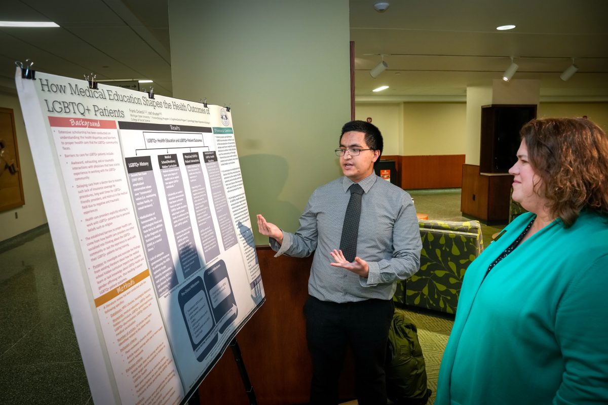 A student presents research from a poster board to Bess German, Assistant Dean of the Honors College.