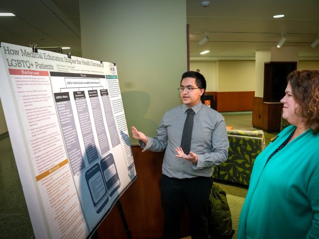 A student presents research from a poster board to Bess German, Assistant Dean of the Honors College.