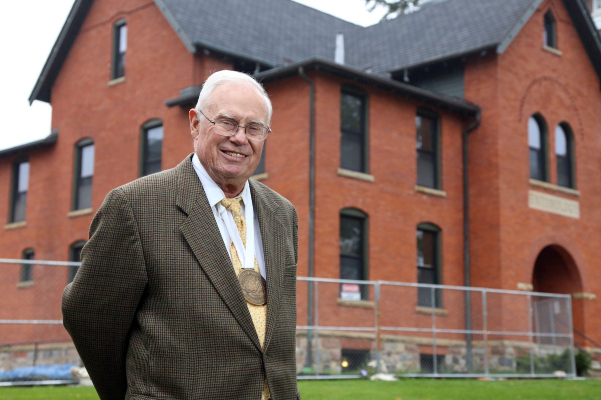 Gary Seevers stands in front of Cook-Seever Hall while it is under construction. Seevers is smiling at the camera, and is wearing a large gold medal around the neck.