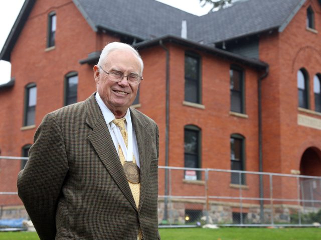 Gary Seevers stands in front of Cook-Seever Hall while it is under construction. Seevers is smiling at the camera, and is wearing a large gold medal around the neck.