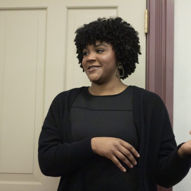 Image of Honors College student Laura-Simone Martin presenting at the 2024 Honors Giving Back Awards. Martin is in black business professional attire and gesturing.