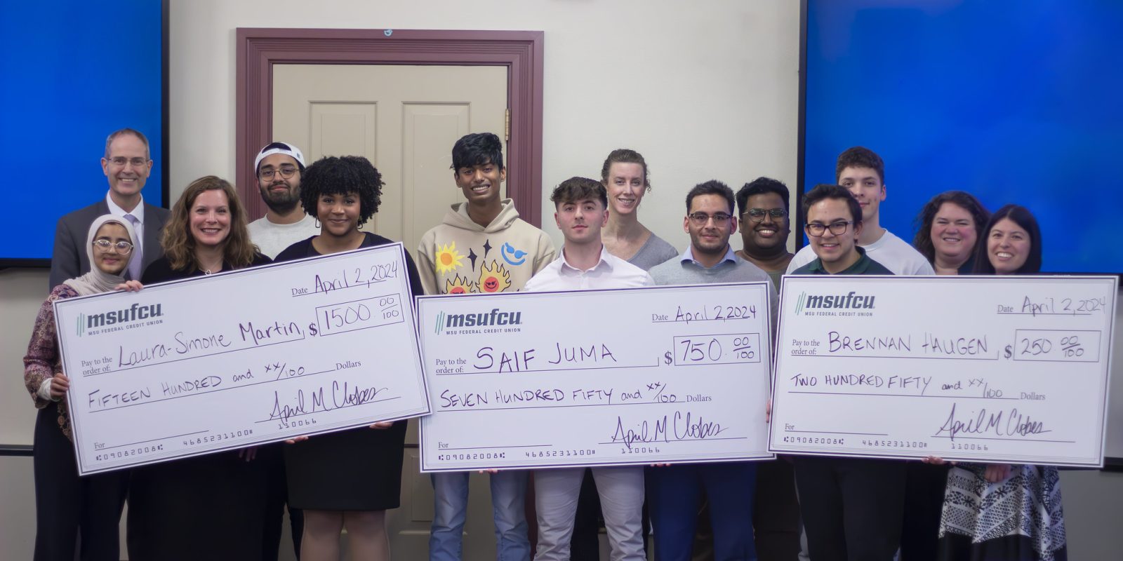 Image of a group of primarily Honors College students and staff standing in front of two blue TV screens.