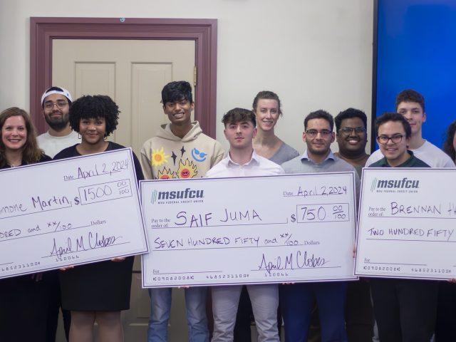 Image of a group of primarily Honors College students and staff standing in front of two blue TV screens.