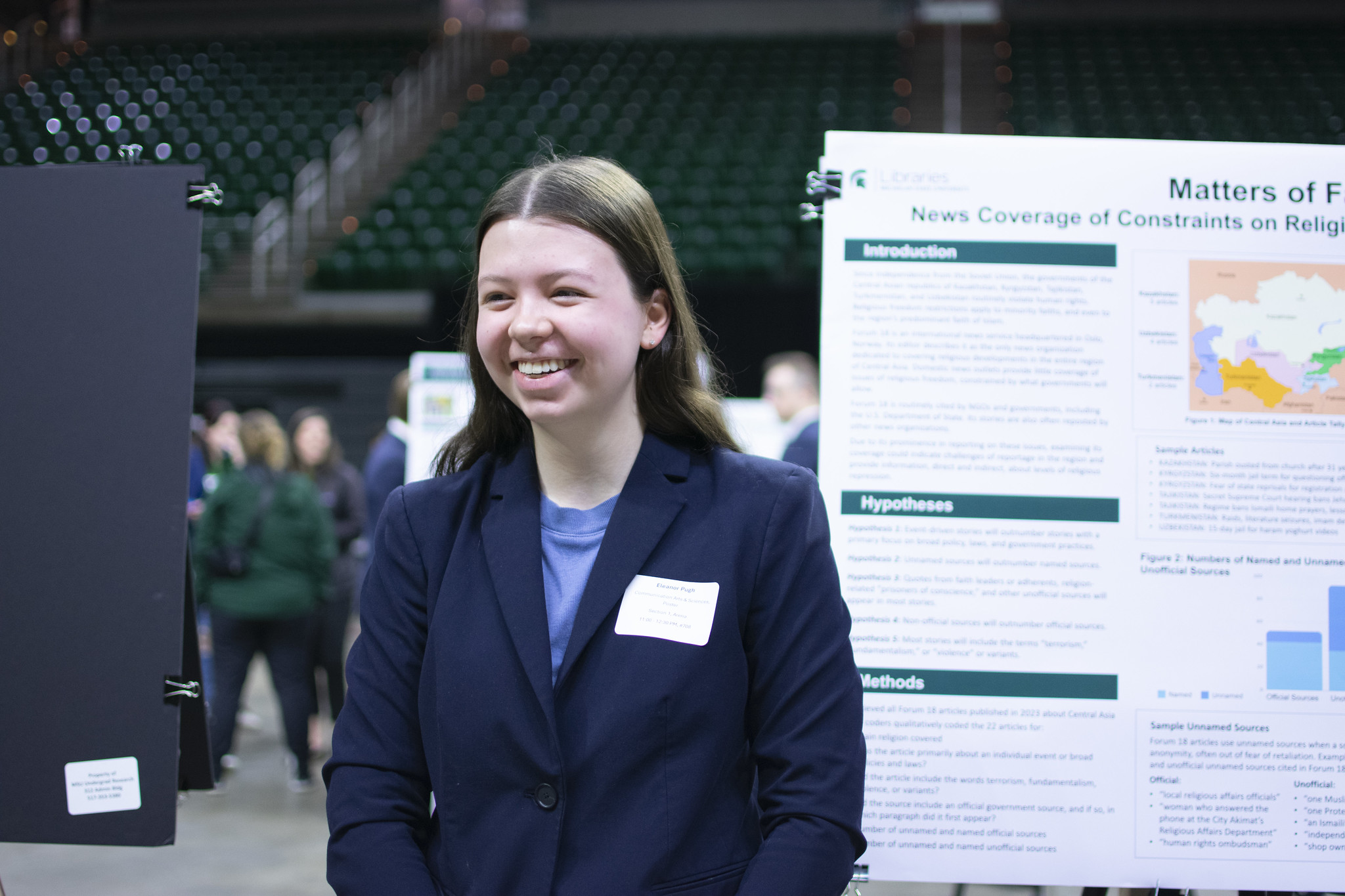 Image of Honors College student Eleanor Pugh smiling in front of a poster at the Michigan State University Undergraduate Research and Arts Forum. Pugh is in formal attire.