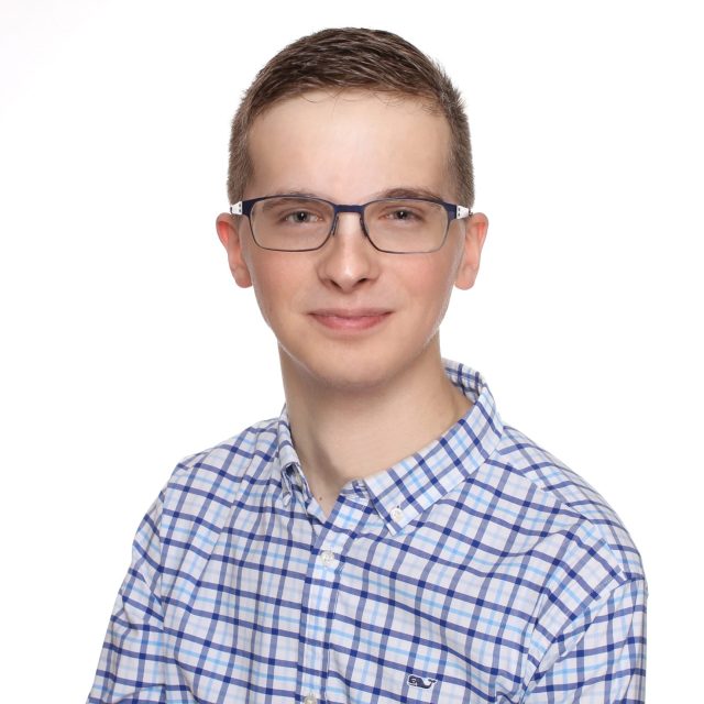 Henry Tighe profile photo wearing glasses and a plaid button-up shirt in front of a neutral white background.