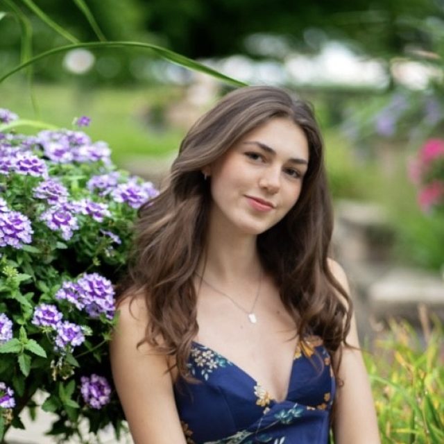 Jolina Huchingson profile photo standing next greenery with purple flowers.