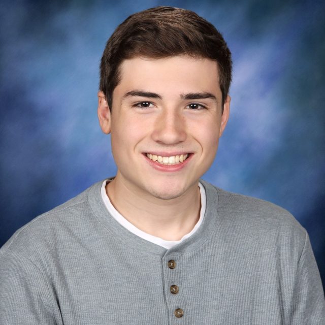 Nathan Guisinger profile photo wearing a gray shirt in front of a blue background.