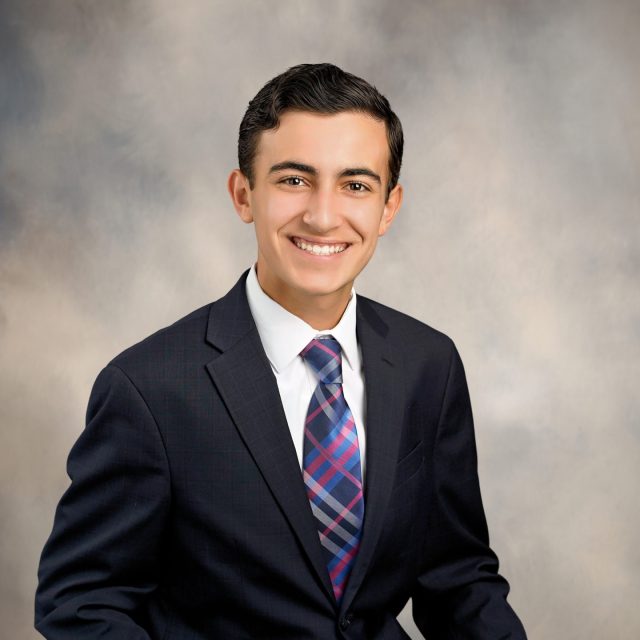 Allesio LoBello profile photo wearing a black suit and a purple-striped tie, sitting in front of a neutral gray background.