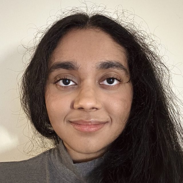 Amrita Renduchintala profile photo wearing a gray turtleneck in front of an off-white background.