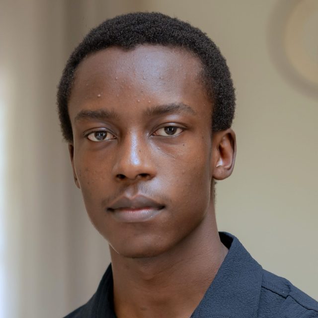 Ethan Tyaba Kigundu profile photo wearing a black shirt and standing in front of a neutral beige background.