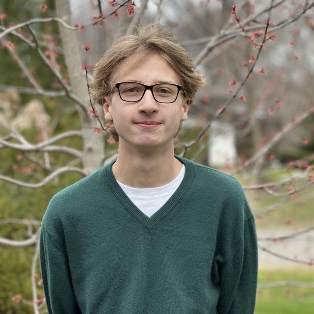 John Cobb profile photo wearing a green sweater and standing in front of a tree with red berries.