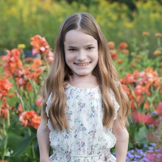 Kaela Laurin profile photo wearing a white dress and standing in a field of colorful flowers.