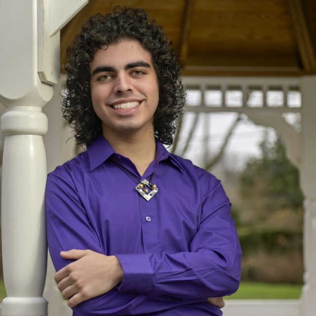 Kieran Venugopal profile photo wearing a purple button-up shirt and leaning against a white column.