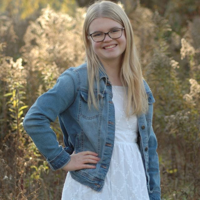 Mary Catherine Leahy profile photo wearing a white dress and jean jacket standing in a forest.