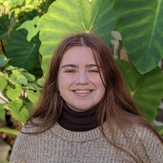 Sophia Bradley profile photo wearing a beige sweater with greenery in the background.