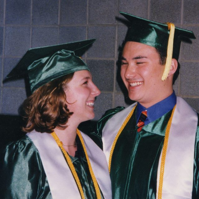 Image of Michigan State University alumni Randy and Michelle Kimple grinning at each other in green college graduation caps and gowns.
