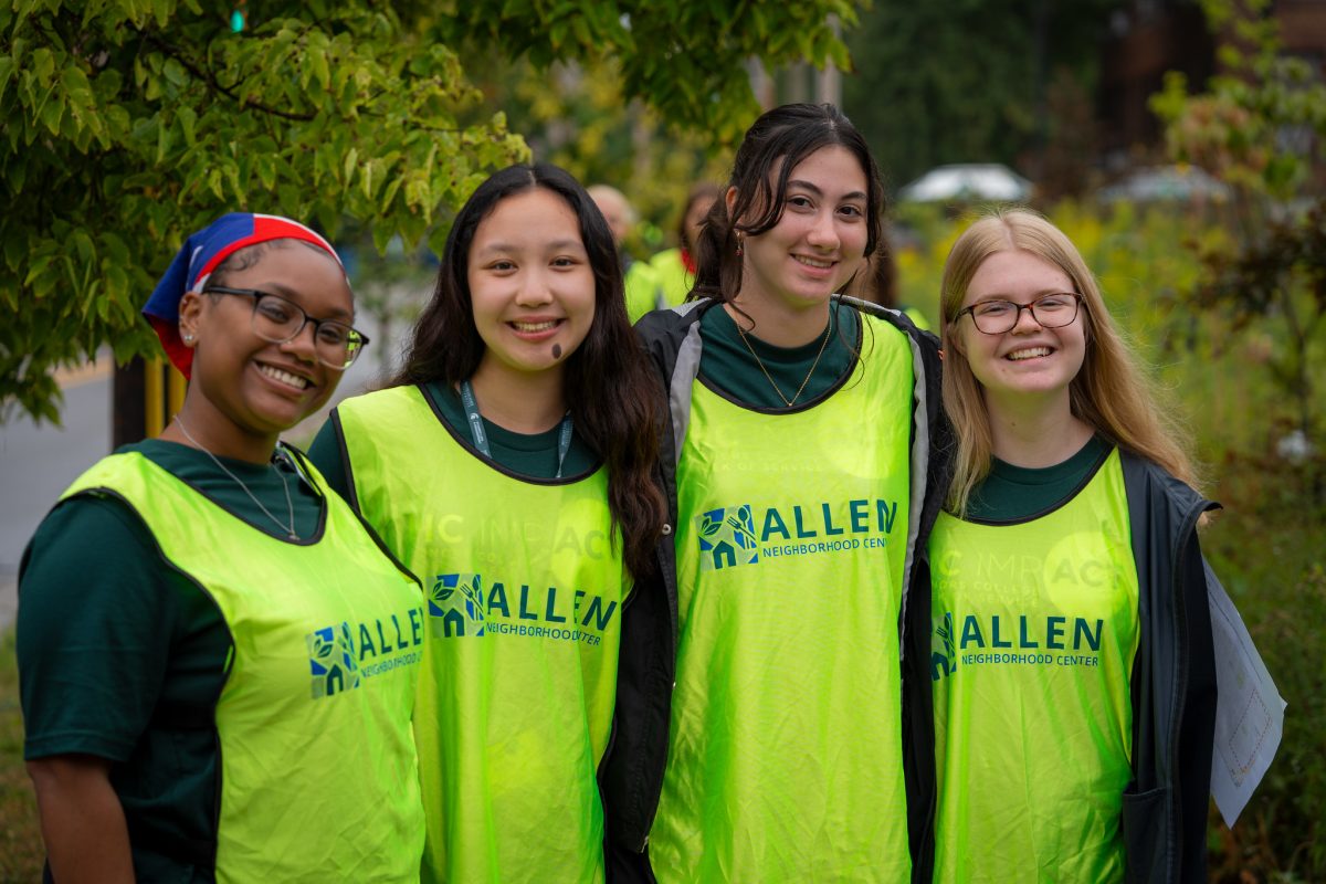 HC IMPACT participants wearing bright neon green Allen Neighborhood Center vests. They are huddled together and smiling at the camera.