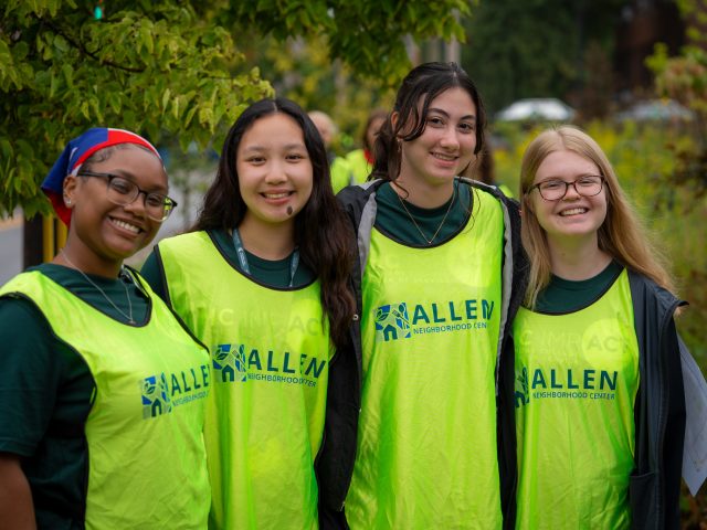 HC IMPACT participants wearing bright neon green Allen Neighborhood Center vests. They are huddled together and smiling at the camera.