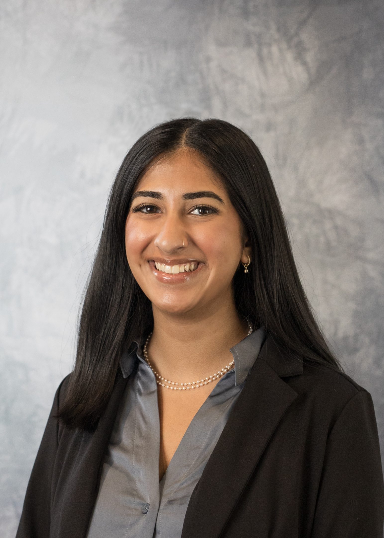 Professional portrait of H-STAR leader and current Michigan State University student Anusha Pandaya smiling in a black cardigan and grey collared shirt. A grey gradient design serves as the background.