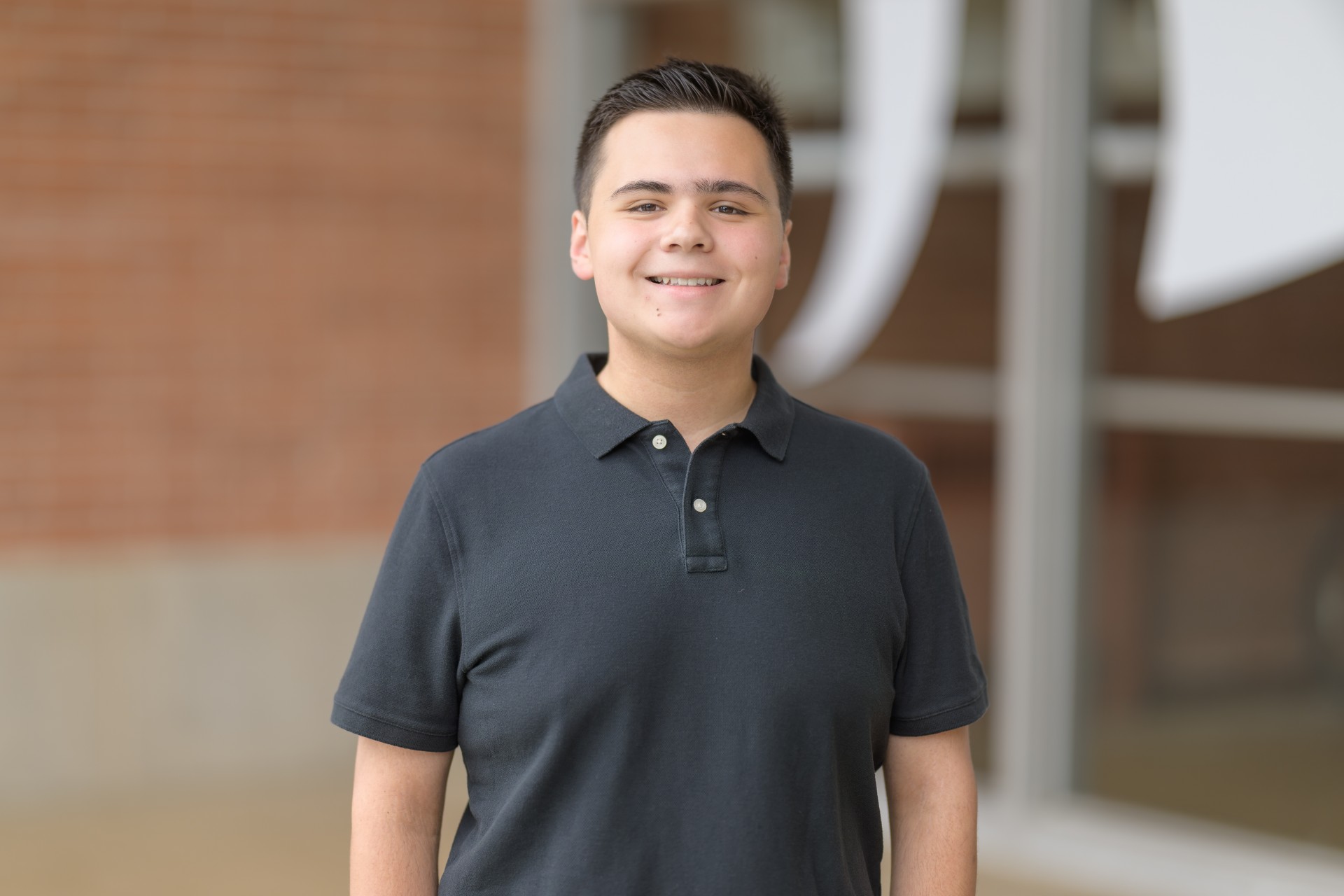 Professional portrait of H-STAR leader and current Michigan State University student Joey Paras standing and smiling. Paras is in a black polo shirt. A red brick building is in the background.