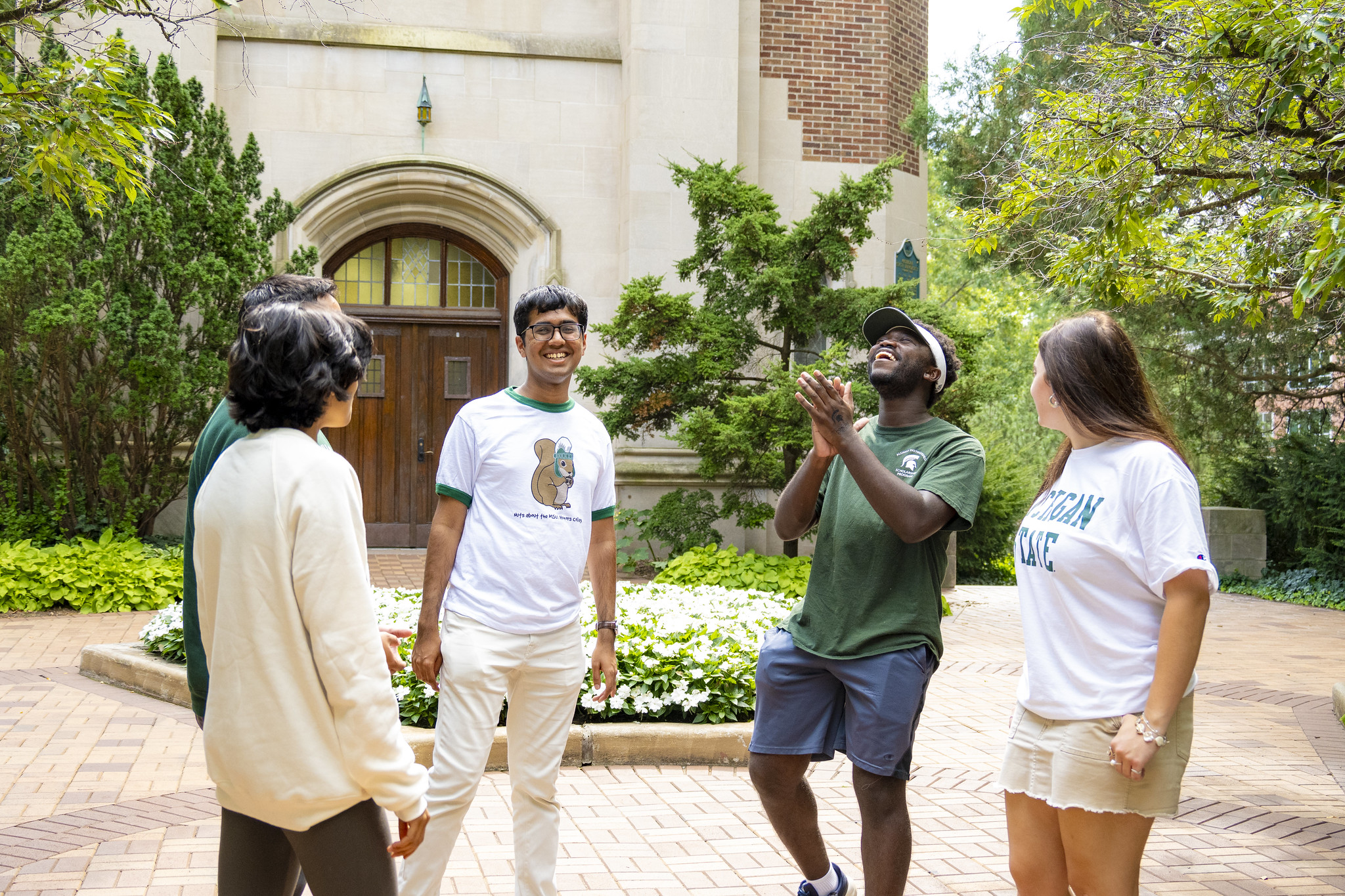 Image of four honors students standing in front of Beaumont tower, wearing msu and honors college clothing and smiling and laughing.