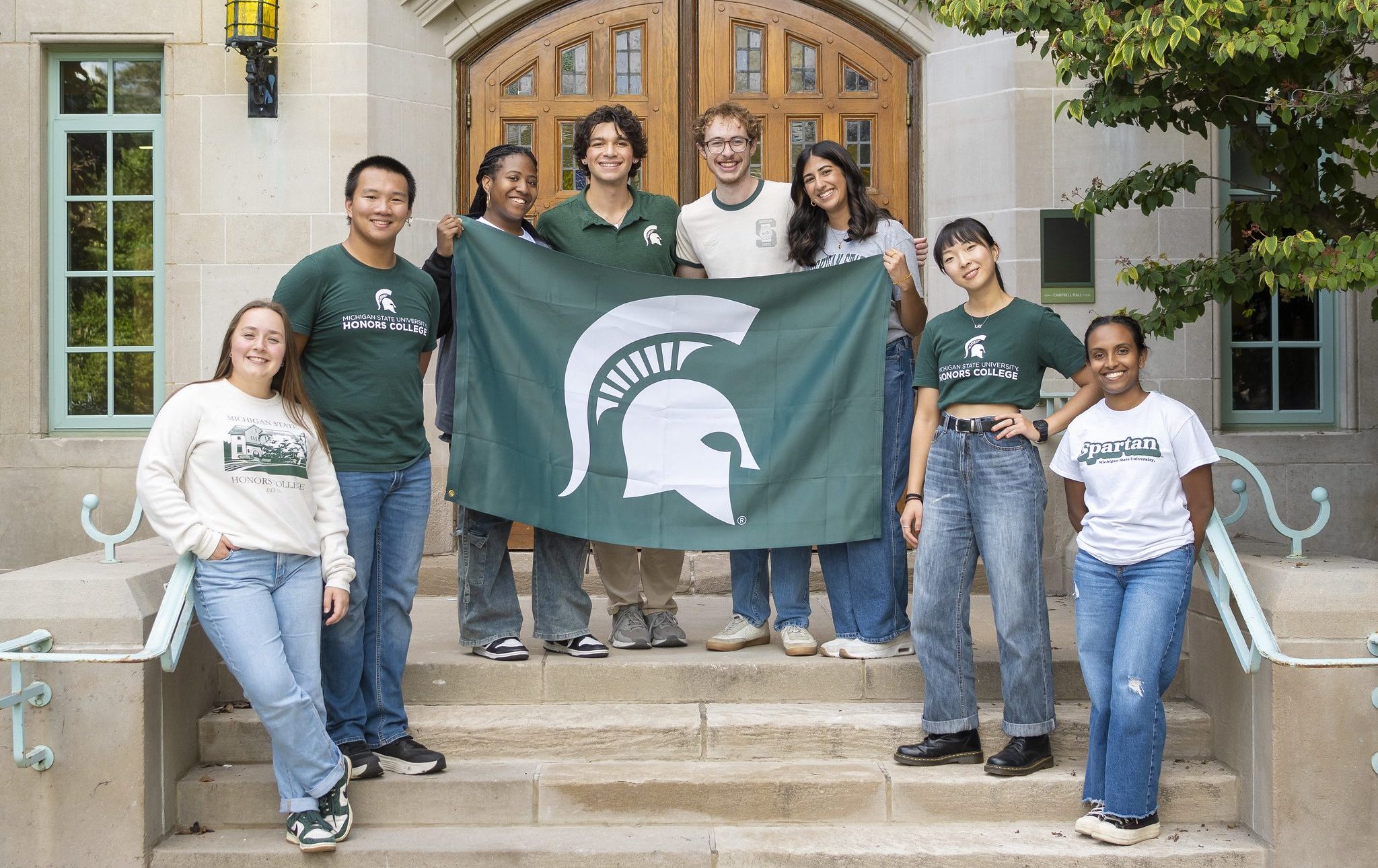 Image of eight honors students in msu and honors clothing standing on the steps of Campbell Hall