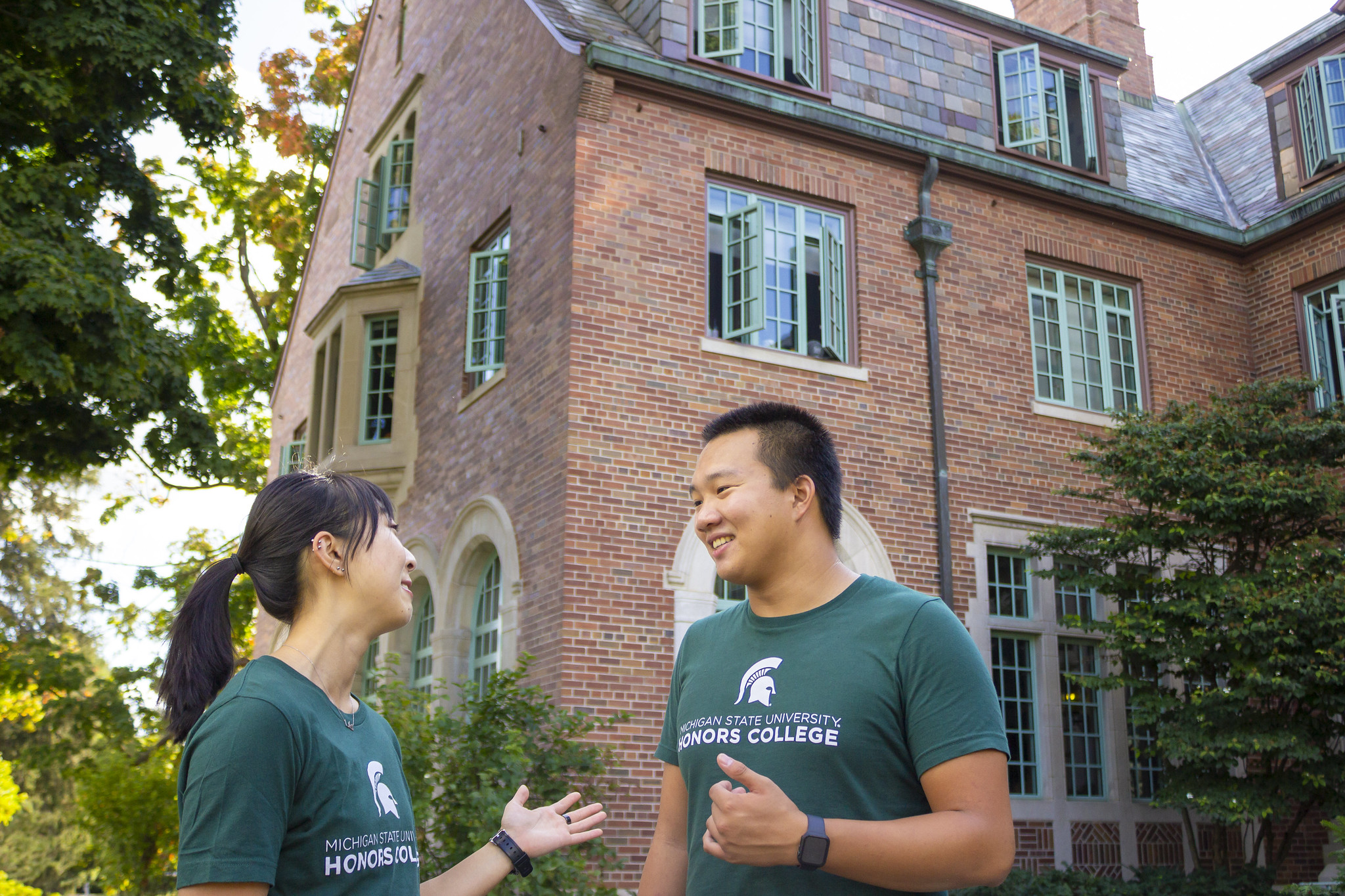 Image of two honors students standing outside Campbell Hall and talking and smiling and wearing honors college t-shirts.