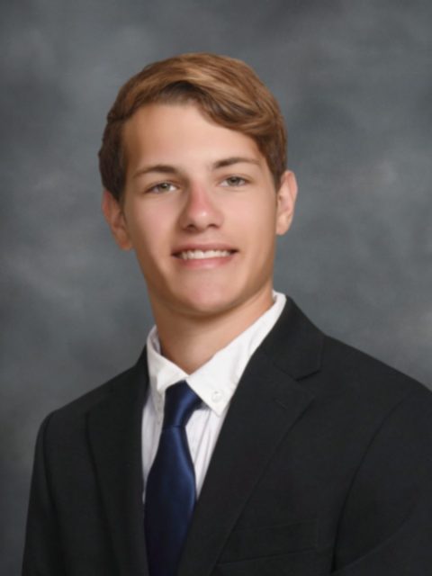 Professional image of incoming MSU Honors College student and Alumni Distinguished Scholar Eric Beswick smiling in a black suit jacket, white collared shirt, and blue tie against a grey gradient background.