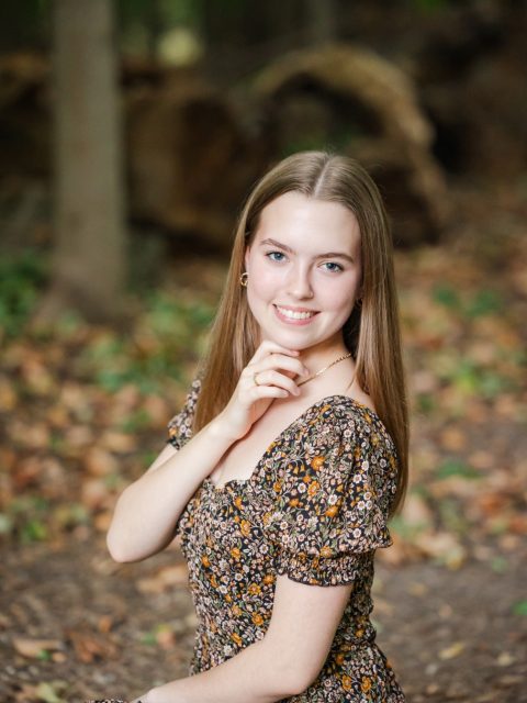 Image of incoming MSU Honors College student and Alumni Distinguished Scholar Violet McKay smiling and crouched on a dirt trail in black, white, and orange floral sundress.
