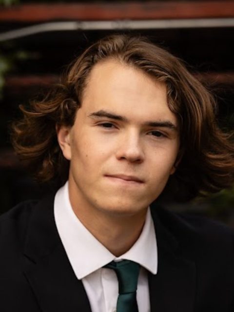 Image of incoming MSU Honors College student and Alumni Distinguished Scholar Alex Morrison with a pensive expression. Morrison is in a black suit jacket, white collared shirt, and dark green tie.
