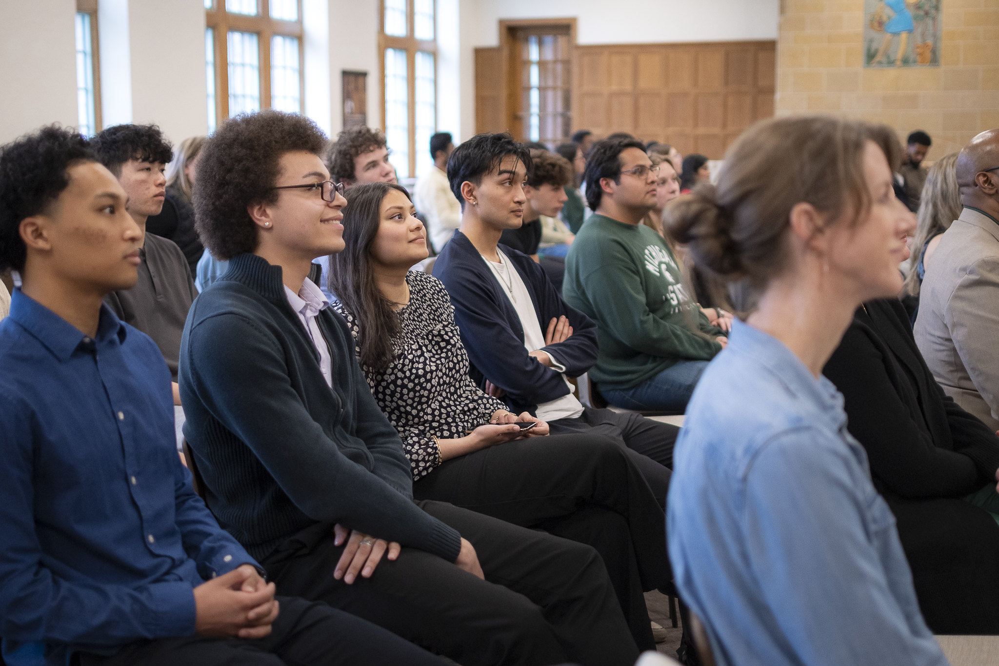 Image of Marcos Garcia (middle row, second from left) sitting and smiling in a crowd inside the Porteous Grand Hall on Michigan State University’s campus for the 2026 Honors Giving Back Awards.