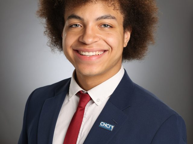 Professional image of Michigan State University student Marcos Garcia smiling in a navy blazer, white collared shirt, and red tie. The background is a gray gradient.
